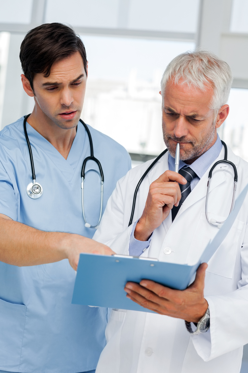 A doctor in a white coat and another doctor in light blue scrubs reviewing notes in a folder