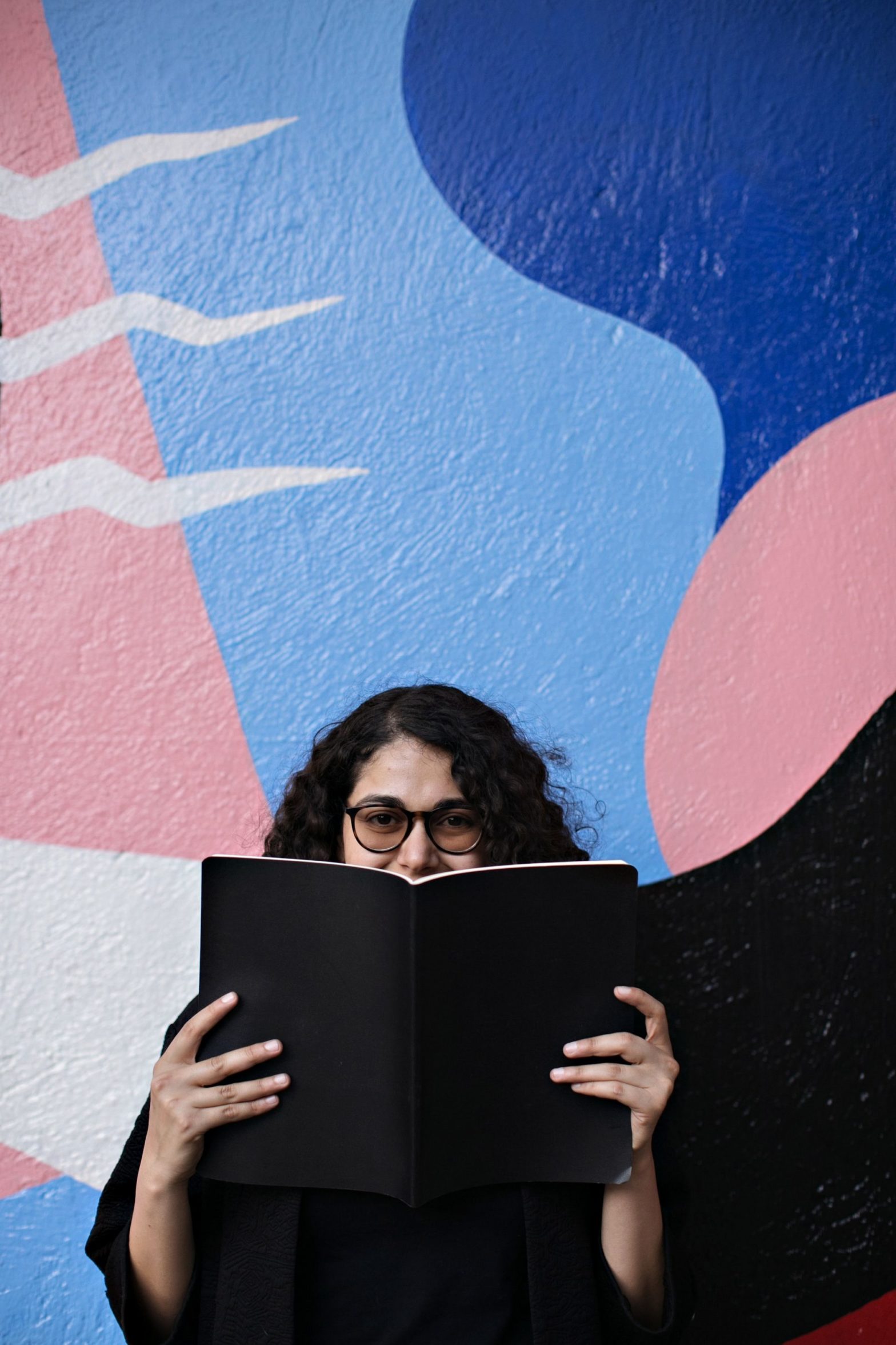 Woman holding a black book in front of a multi-colored background