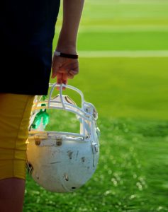 A hand holding a football helmet on a grass field