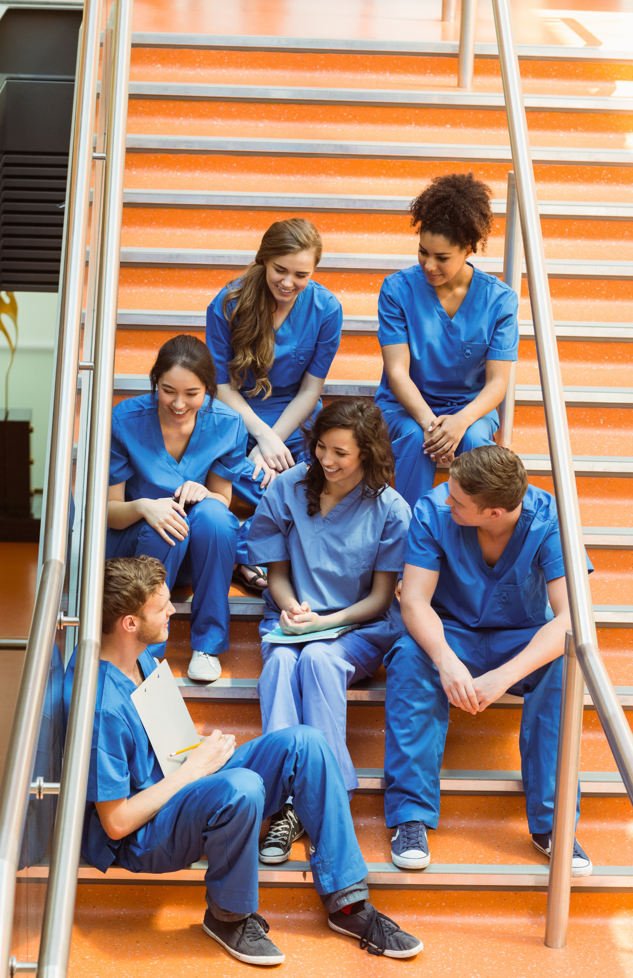 Six doctors in blue scrubs sitting on orange stairs
