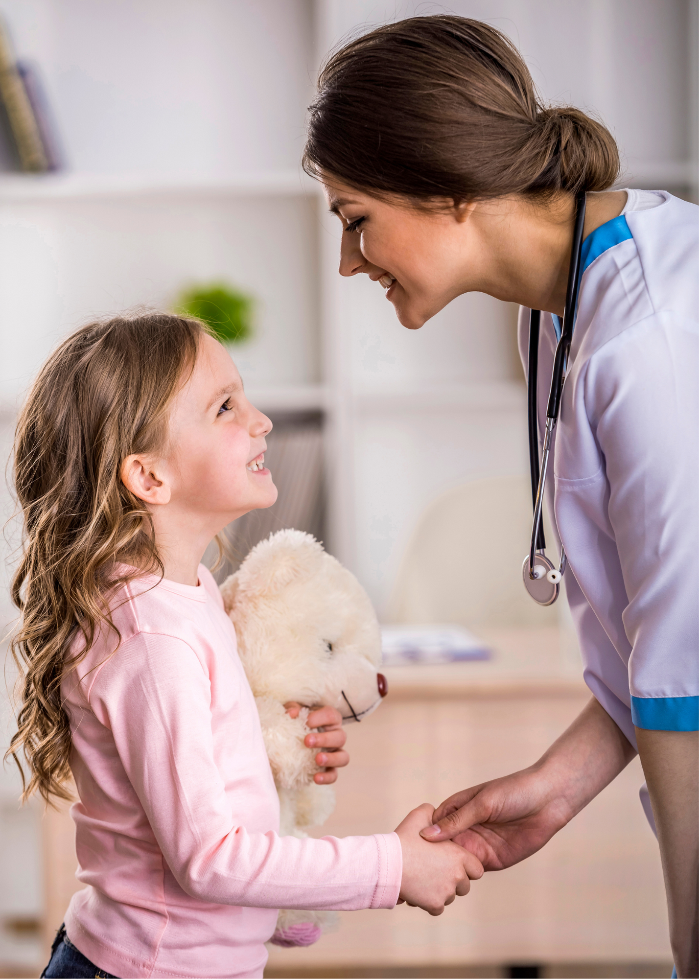 A female doctor shaking hands with a female child holding a teddy bear
