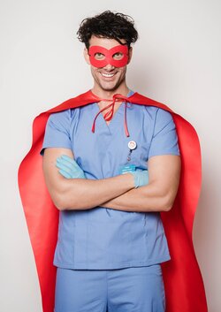 A male doctor in blue scrubs with a red superhero mask and red cape