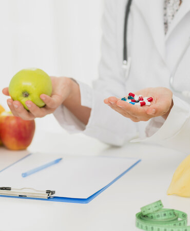 A doctor in a white coat holding a green apple in one hand and pills in their other hand