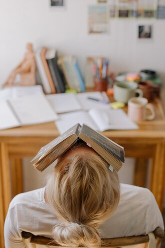 Student at a desk with an open book resting on their face