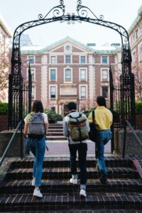 Three students walking up brick stairs towards a brick school