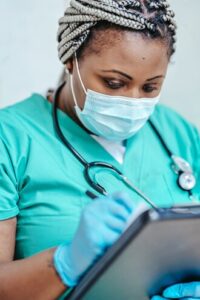Woman in green scrubs with a medical mask writing on a clipboard